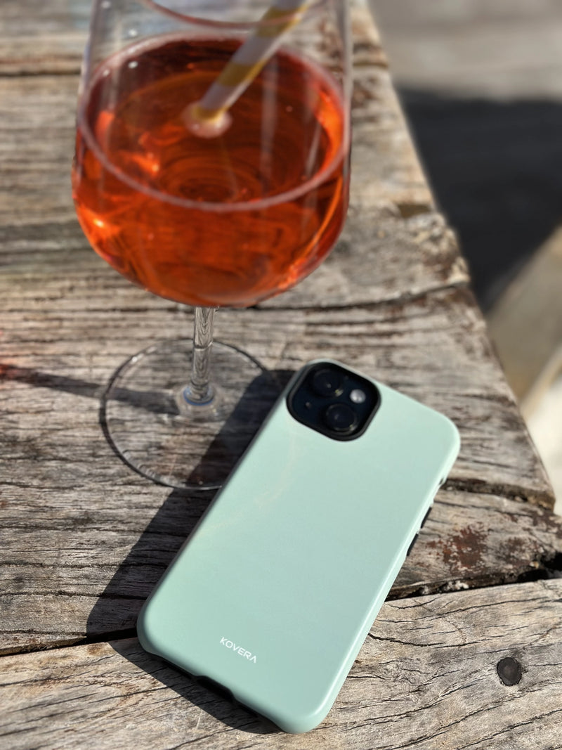 Ochranný kryt na iPhone Kovera položený na stole vedľa pohára vína, reálne používanie obalu na mobil v exteriéri