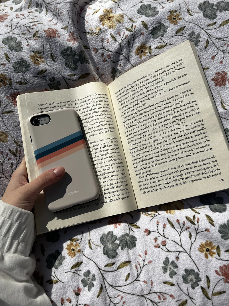 Ochranný kryt na iPhone Kovera v reálnom použití, mobil položený na otvorenej knihe, minimalistický dizajn obalu na mobil v domácom prostredí
